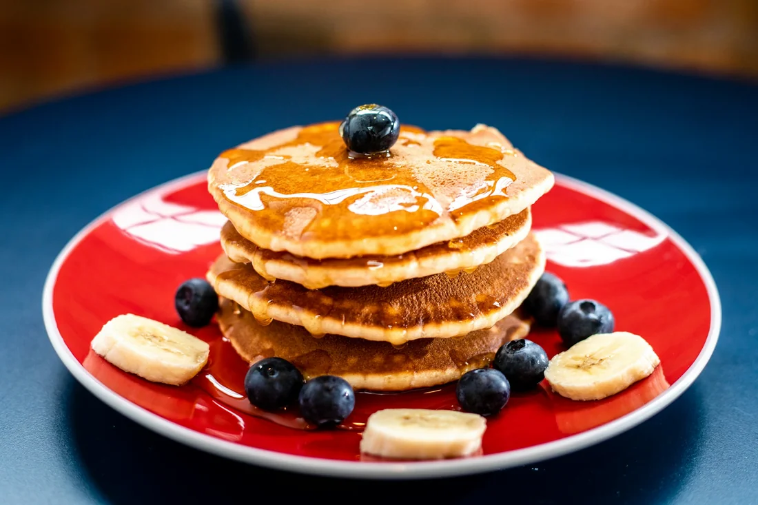 Golden pancakes with fruit on a bright red plate